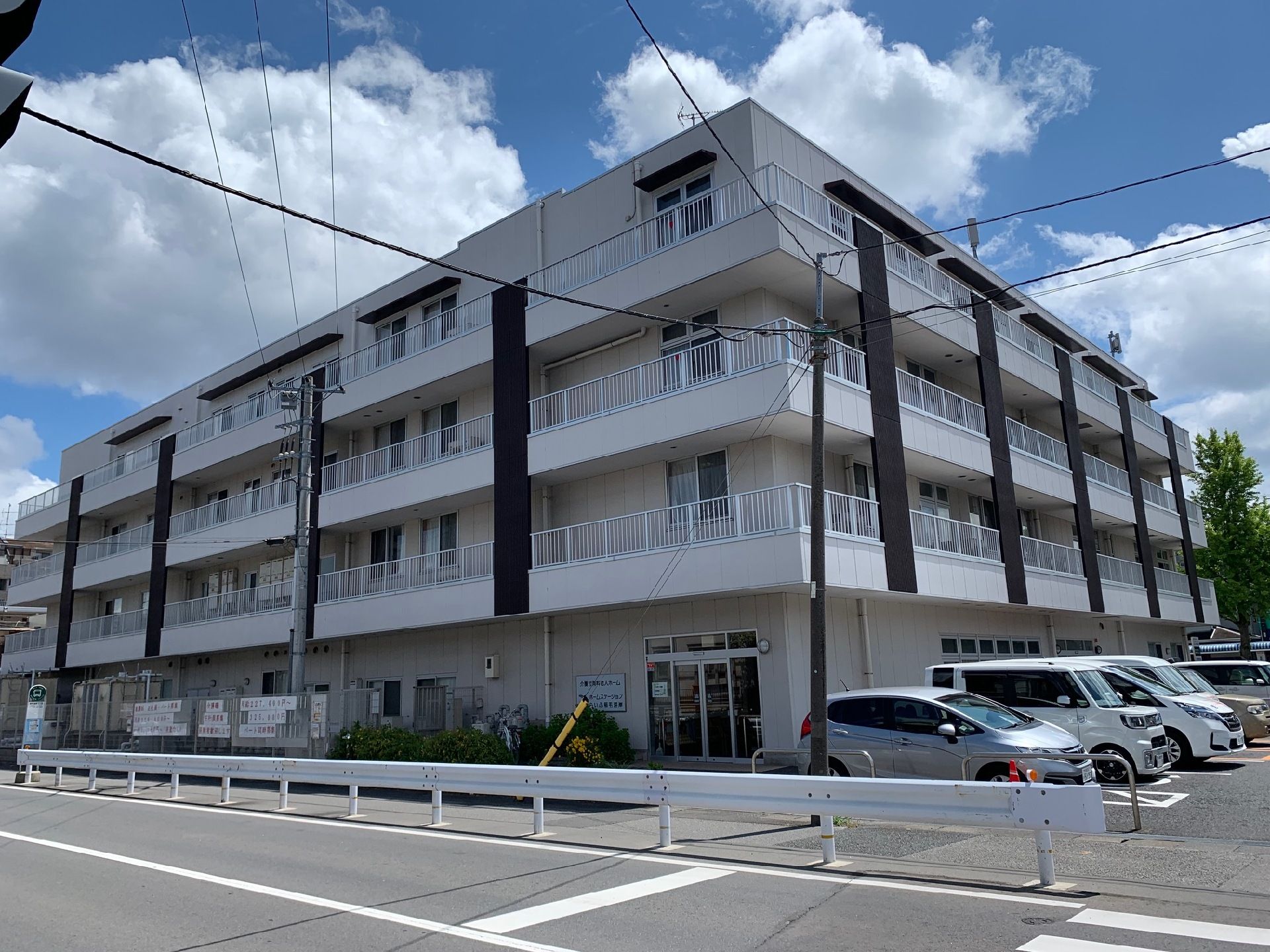 建物の前に駐車場を備えている白っぽい外観の高齢者施設