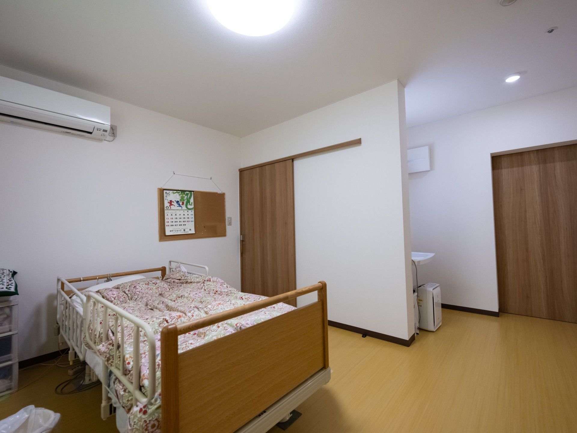 右手前にシャワーヘッドのついた洗面台があり、介護ベッドが置かれた居室