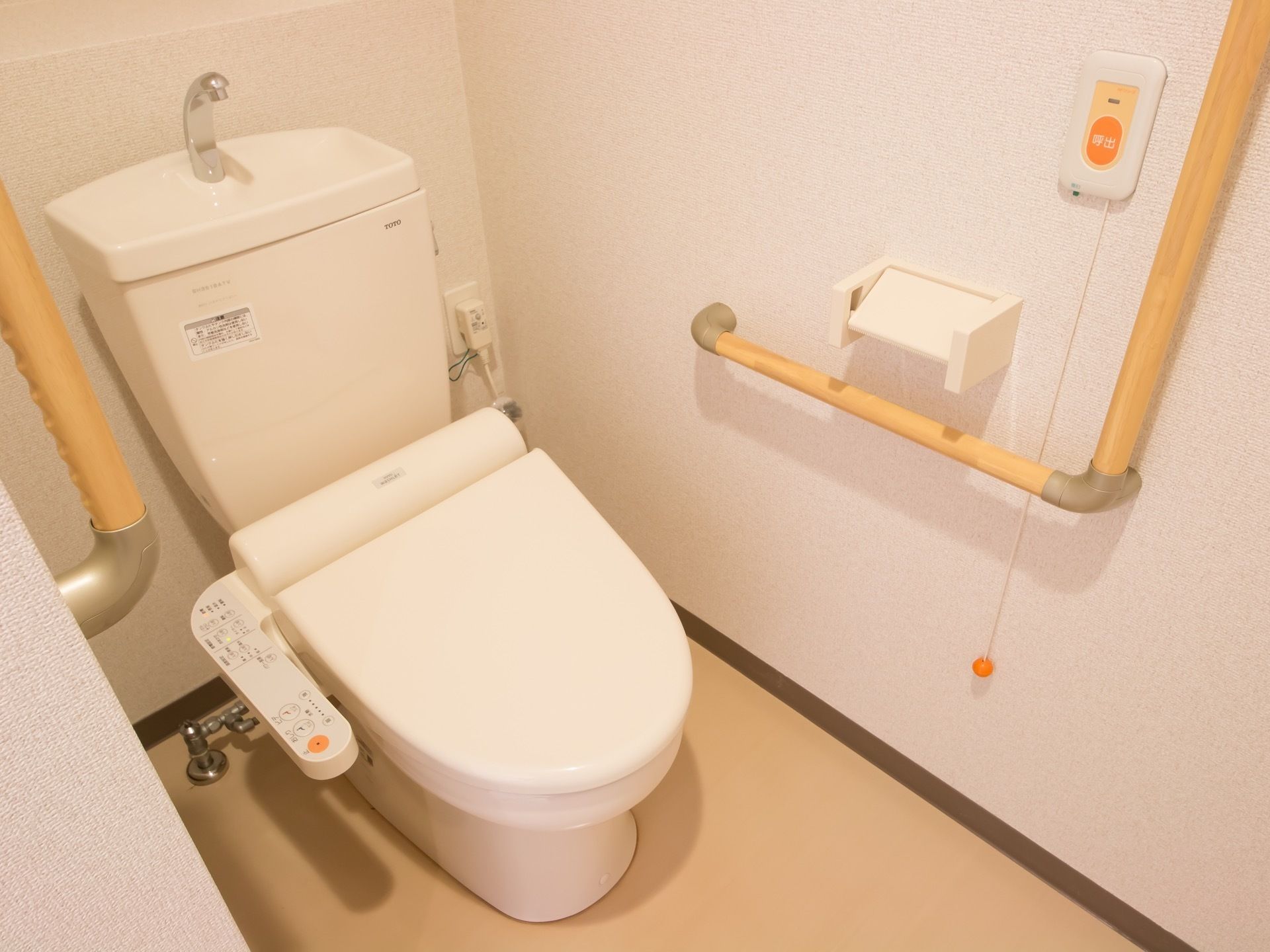 便座の両側の壁に、I字型とL字型の手すりが設置されている。緊急通報装置がL字型の手すりの側についている。