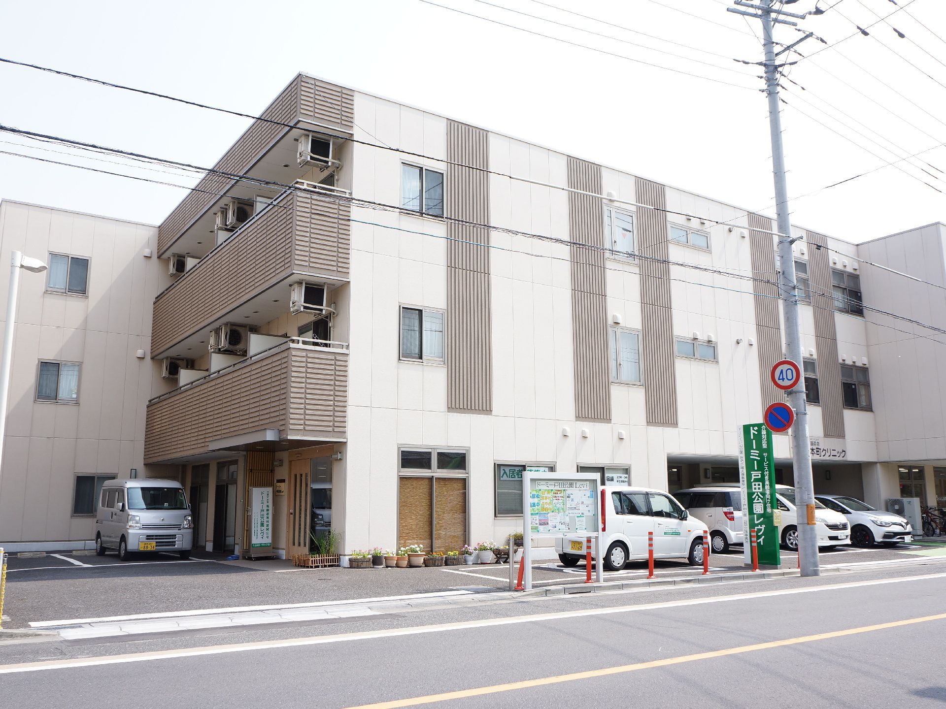 玄関前に軽自動車が停まった駐車場があり、大通に面している施設の外観