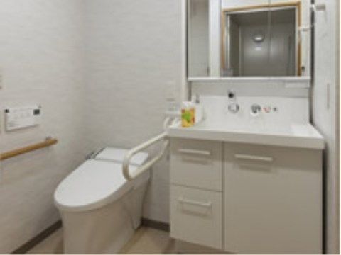 洗面台の隣に洋式トイレが設置されている。トイレの横に跳ね上げ式の補助バーが、壁に手すりが取り付けられている。