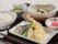 天ぷらを盛り付けた皿があり、周りにご飯、煮物、小鉢、漬物が並べられている。天ぷらはえび、オクラ、なすの3種類がある。