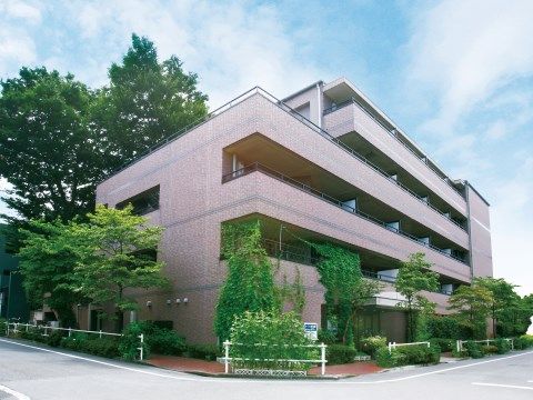 建物周囲がたくさんの樹木で囲まれているピンク色の建物