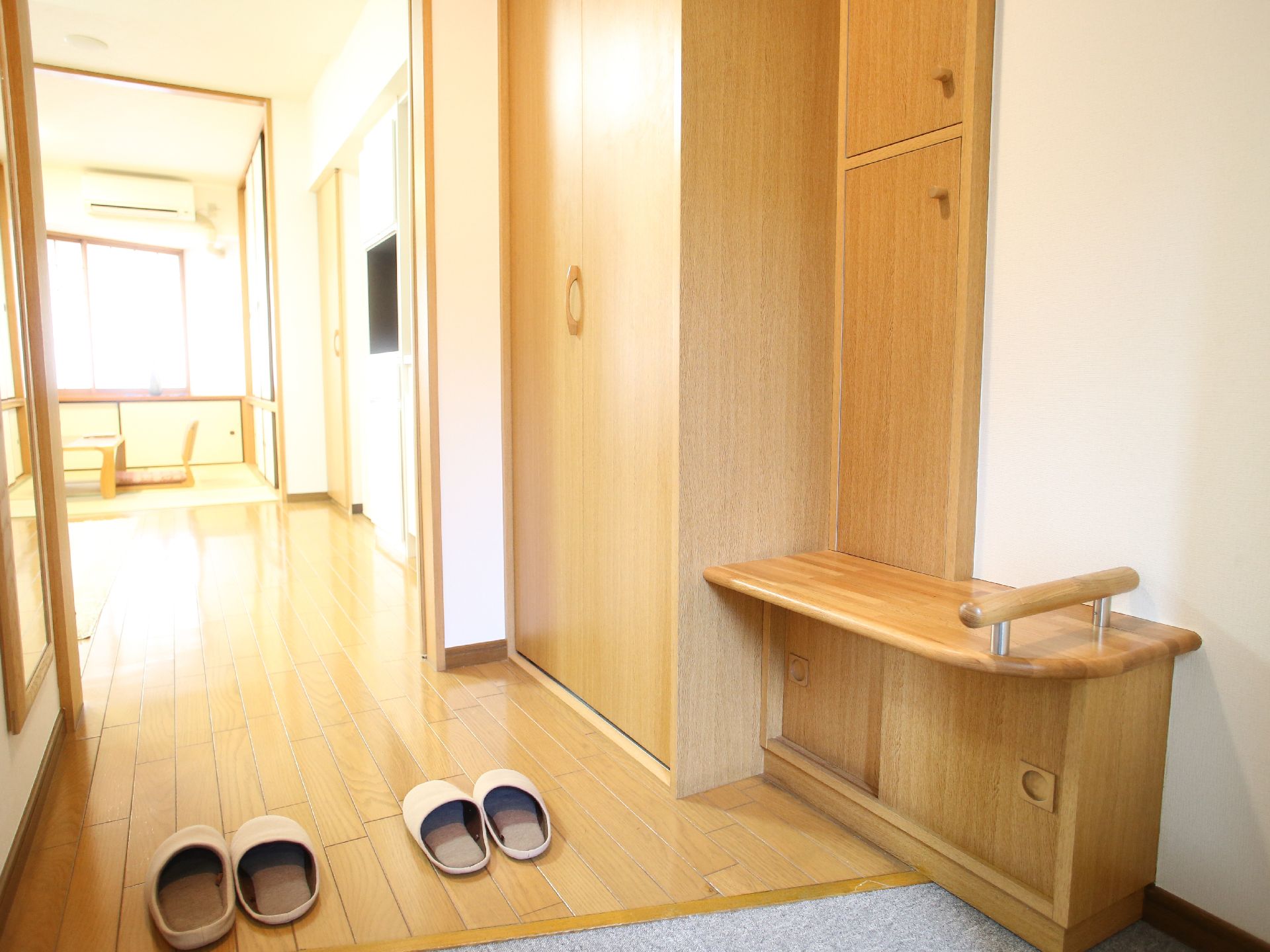木目調を基調とした居室である。上り口には、スリッパを置いている。右側には、収納庫を設置し、奥には和室を備えている。