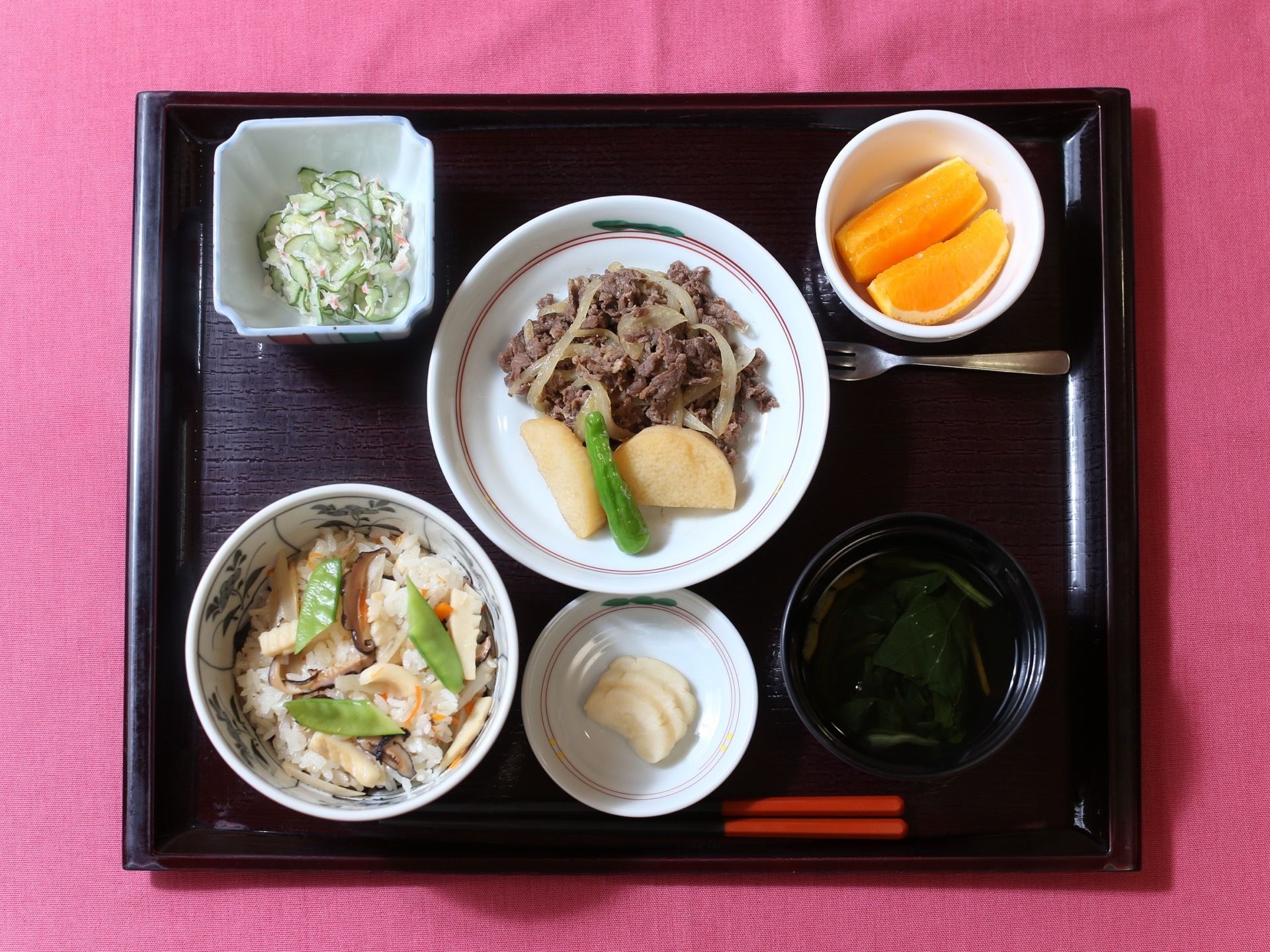 四角のトレーの上に、混ぜご飯とお吸い物に肉のメインおかずである。それにお漬物と小鉢１品、フルーツを添えた食事である。