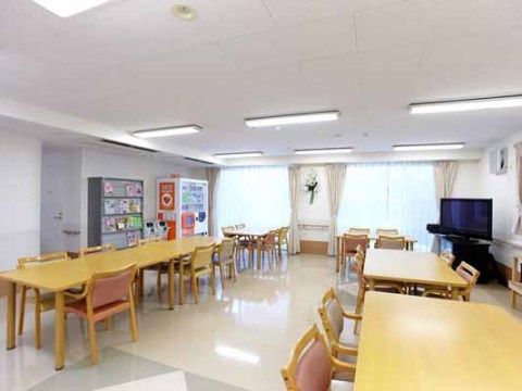 広く開放的な食堂には、ダイニングテーブルが並べられている。大型テレビが窓際に設置されている。壁際に、マガジンラックと自販機が置かれている。