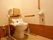 暖色系の照明が使われ、トイレ用肘掛け、背もたれなどの補助器具がついたトイレ。温水洗浄便座が備わっている。