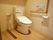 ベージュを基調とした広々としたトイレ。トイレの脇には手すりが取り付けてられている。緊急通報装置も完備