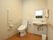 トイレの壁にはL字に手すりが付けてあり、左側には折りたたみタイプの手すりも設置されている。便座の横に手洗い場がある。