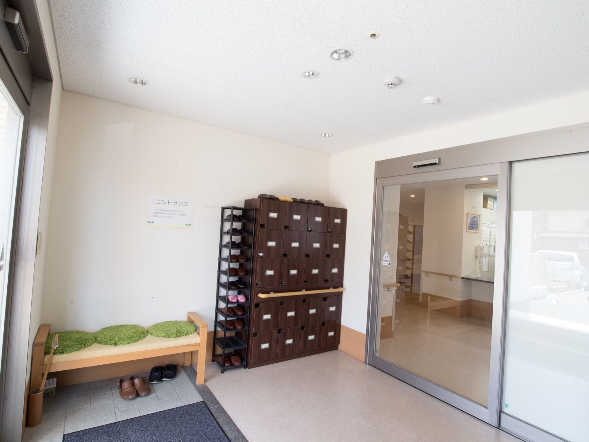 扉付きの個室の靴箱の隣にスリッパラックが置いてある。緑色の丸座布団が敷いてある木のベンチが壁際に設置されている。