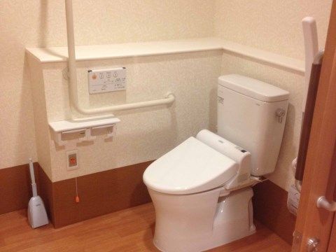 広いスペースがある居室内のトイレ。便器の脇には可動タイプの手すりが設置されている。壁にはナースコールが取り付けられている。