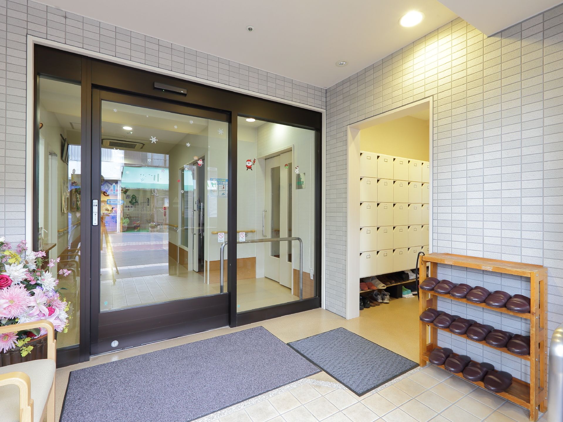 建物のさらに奥に入るのに、自動扉がある。花が飾られている。来客用のスリッパとラックがある。ラック近くに手すりが取り付けられている。