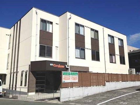 茶色い木製の柵で囲まれている、３階建ての白い建物の外観