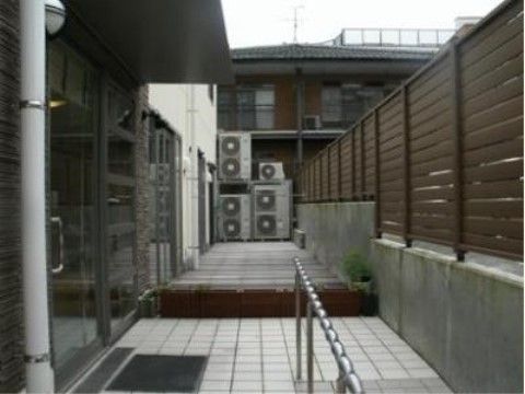 ガラス引き戸の入り口で、前には屋根が設けられている。手すり付きのスロープとつながっており、床はタイル張りになっている。