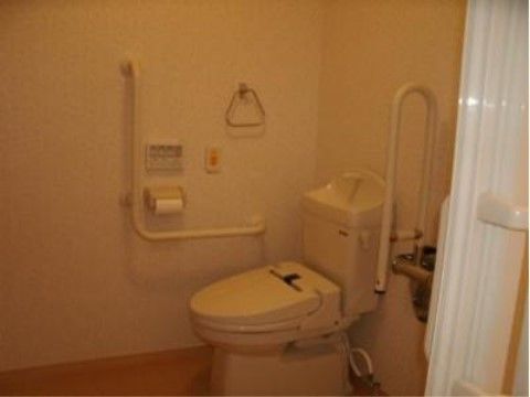 白を基調とした清潔感のあるトイレ。温水洗浄便座が設置されている。便座の近くには手すり、緊急呼出ボタンが設けられている。