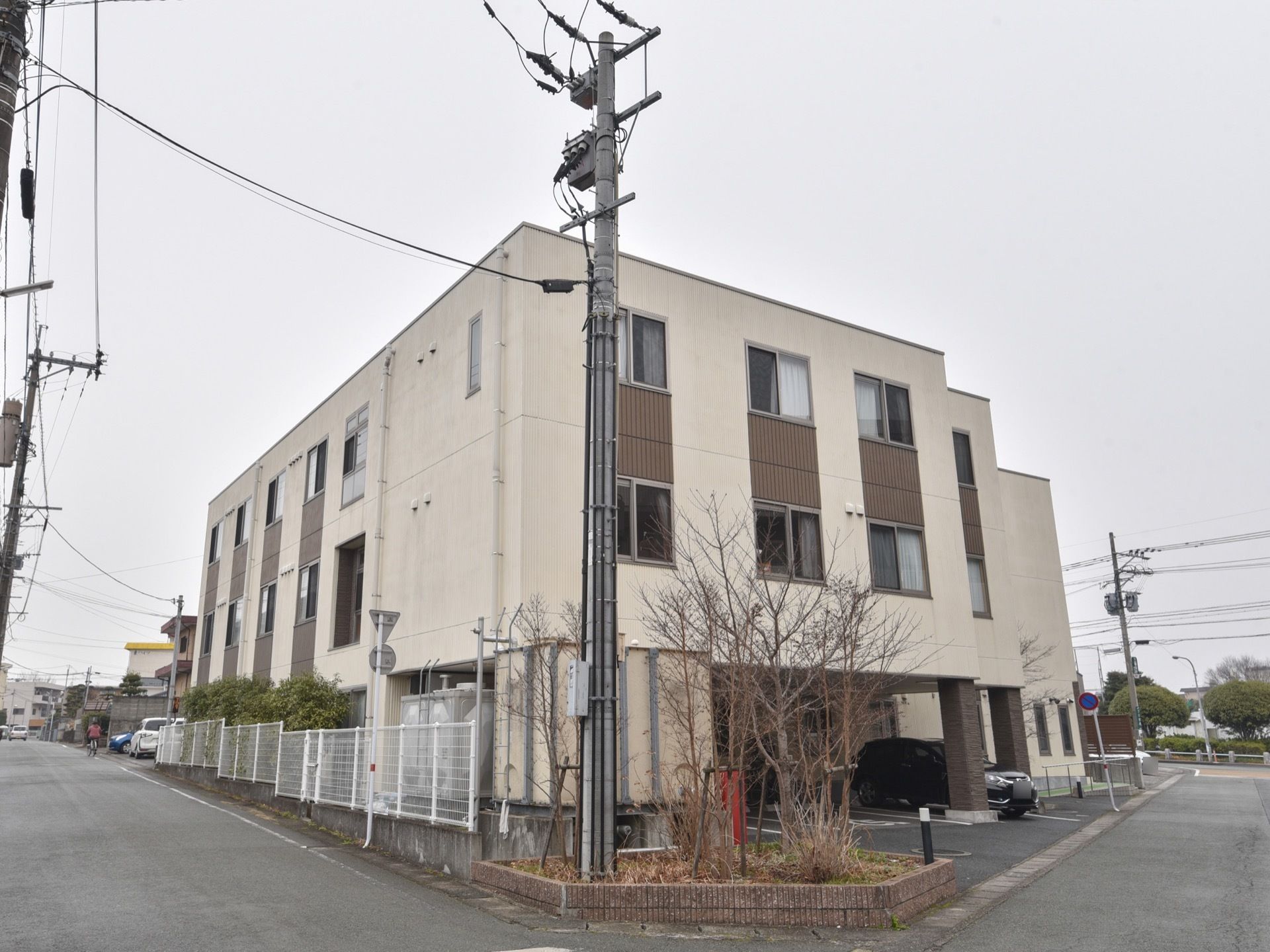 施設の建物は三階建てで、外壁の色は明るいベージュ系である。一階部分に空間を設け、駐車スペースとしている。