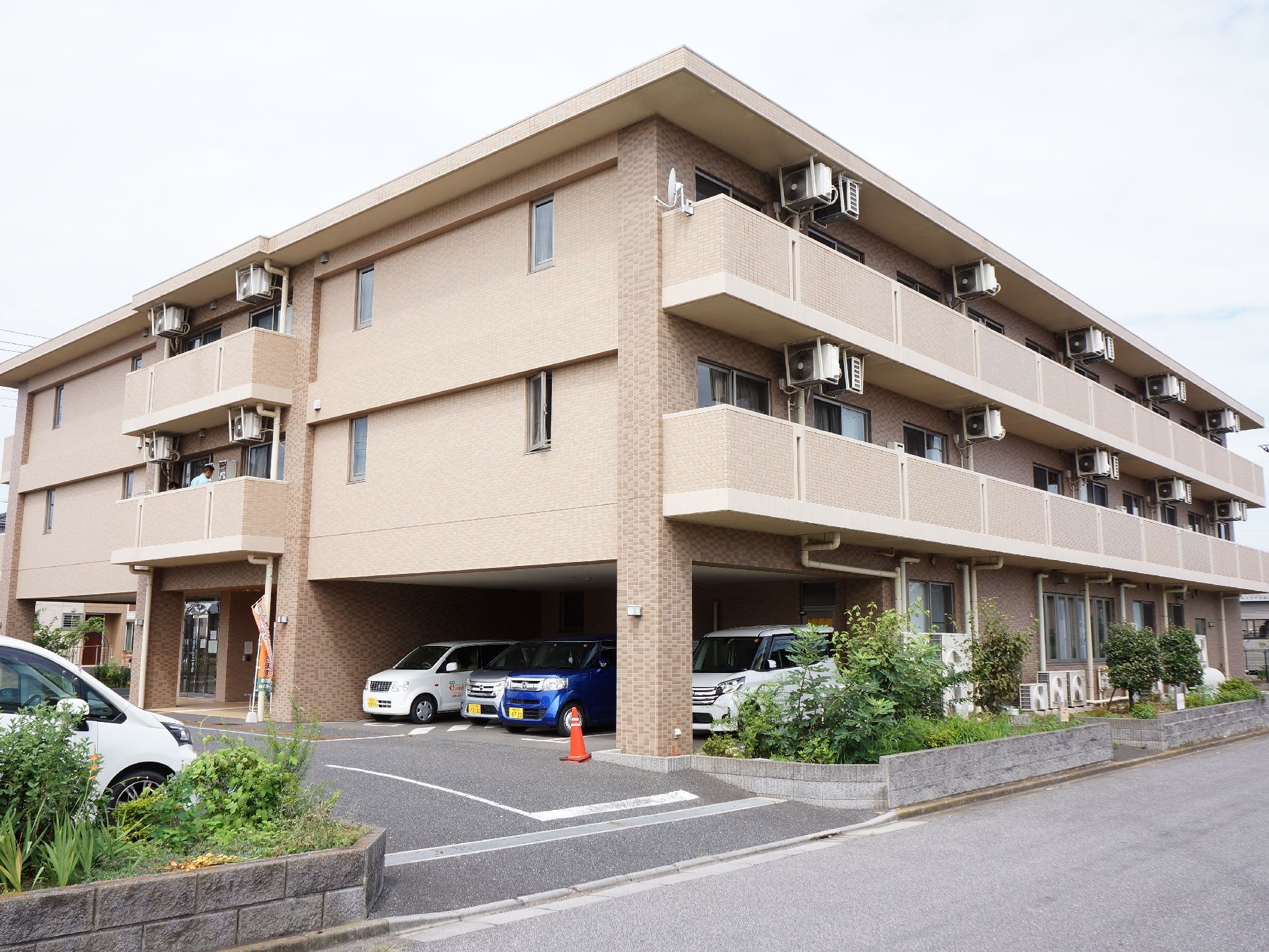 茶色のアパートのような外観のこの建物で、利用者が生活を送る。車をとめることのできるスペースも充実している。