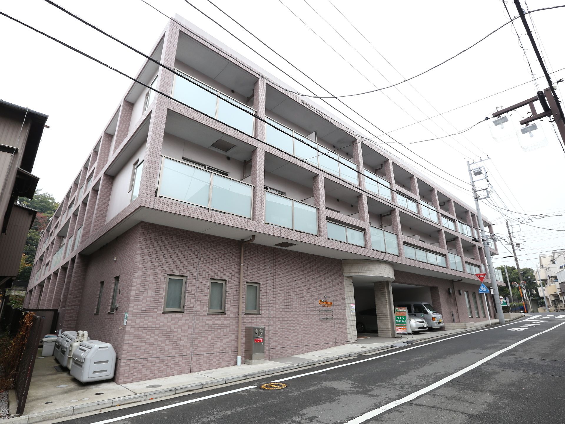 1階は駐車場、2階以上が居住空間になっている。建物の壁に施設名が書かれたプレートが取り付けられている。玄関前に立て看板が置かれている。