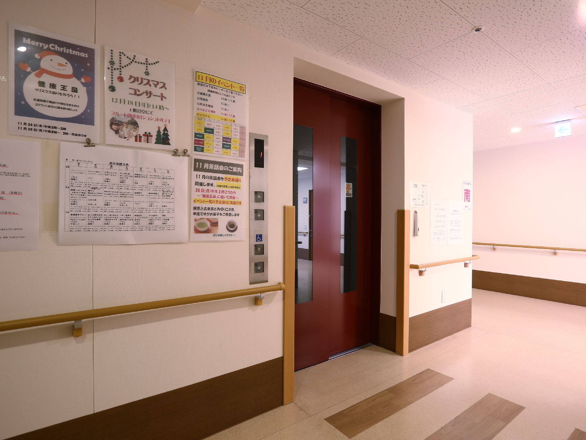 壁に手すりが設置してある。行事のお知らせや食事の献立表が貼ってある。車いすでも乗れる十分な大きさがある。