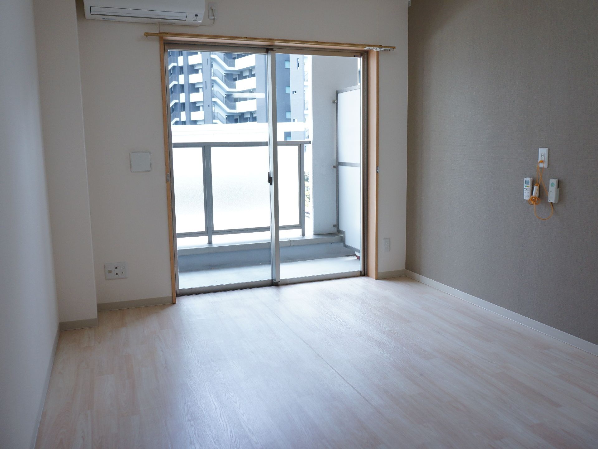 居室は白壁にフローリングの洋室タイプ。奥には広い窓があり大きなガラスで外がよく見える。外はベランダになっていて出入りすることができる。