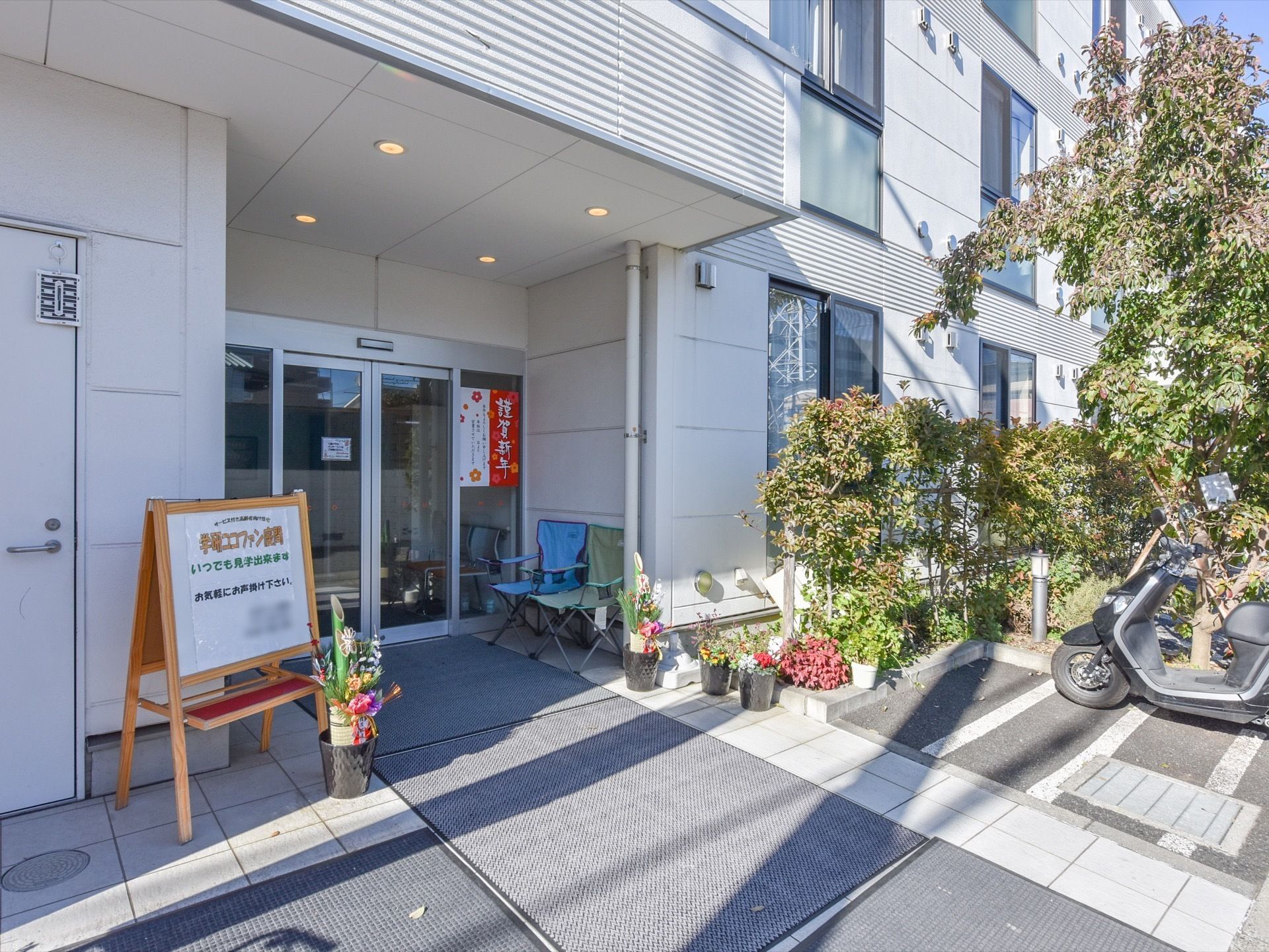 広くて開放的な自動ドアの玄関。たくさんの植物が植えられていて季節を感じる。また、時季に合った装飾がされている。