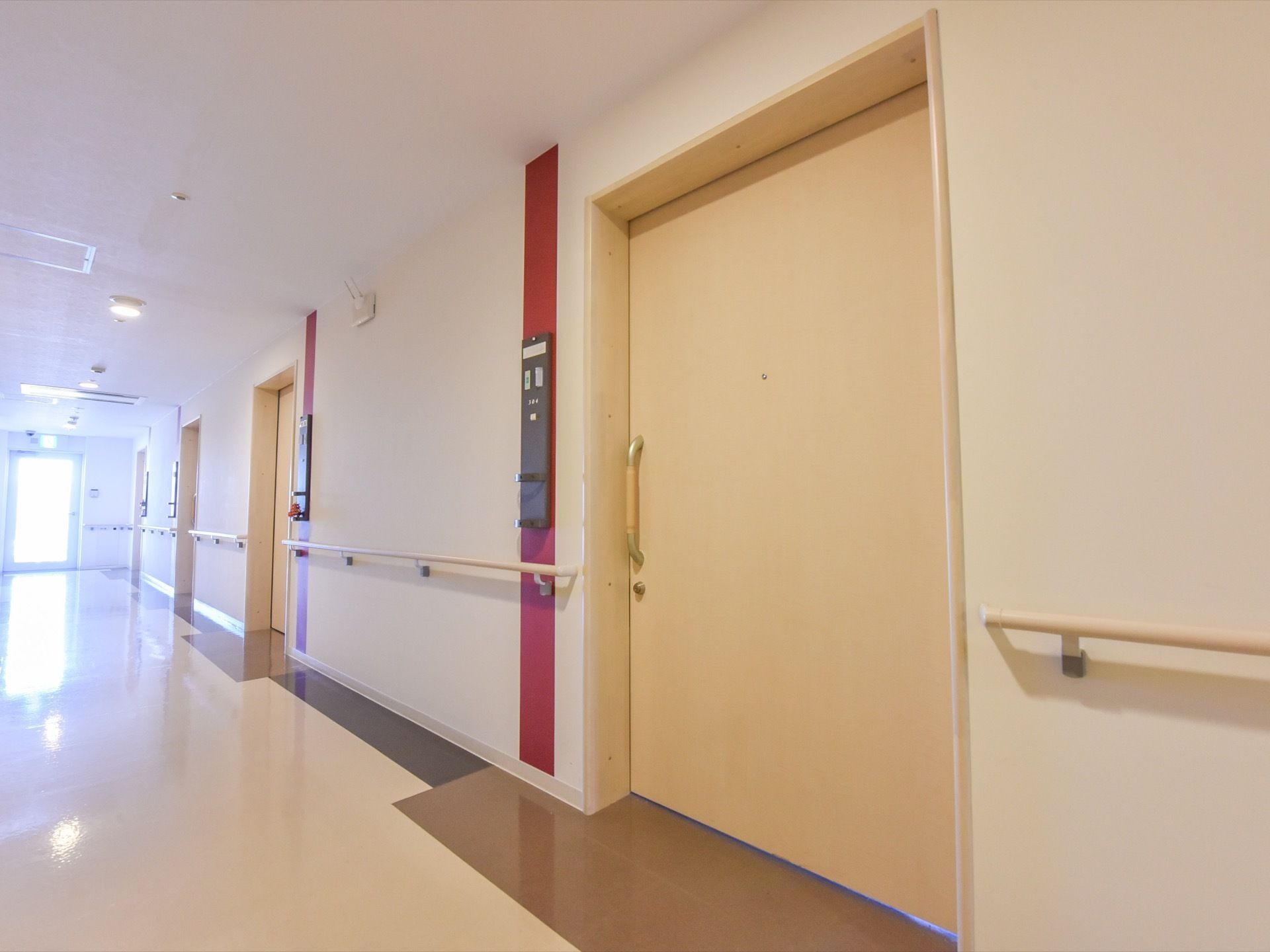 廊下には手すりが続いていて歩行に便利である。入口は引き戸で開けやすい。オフホワイトで統一された落ち着いた雰囲気。