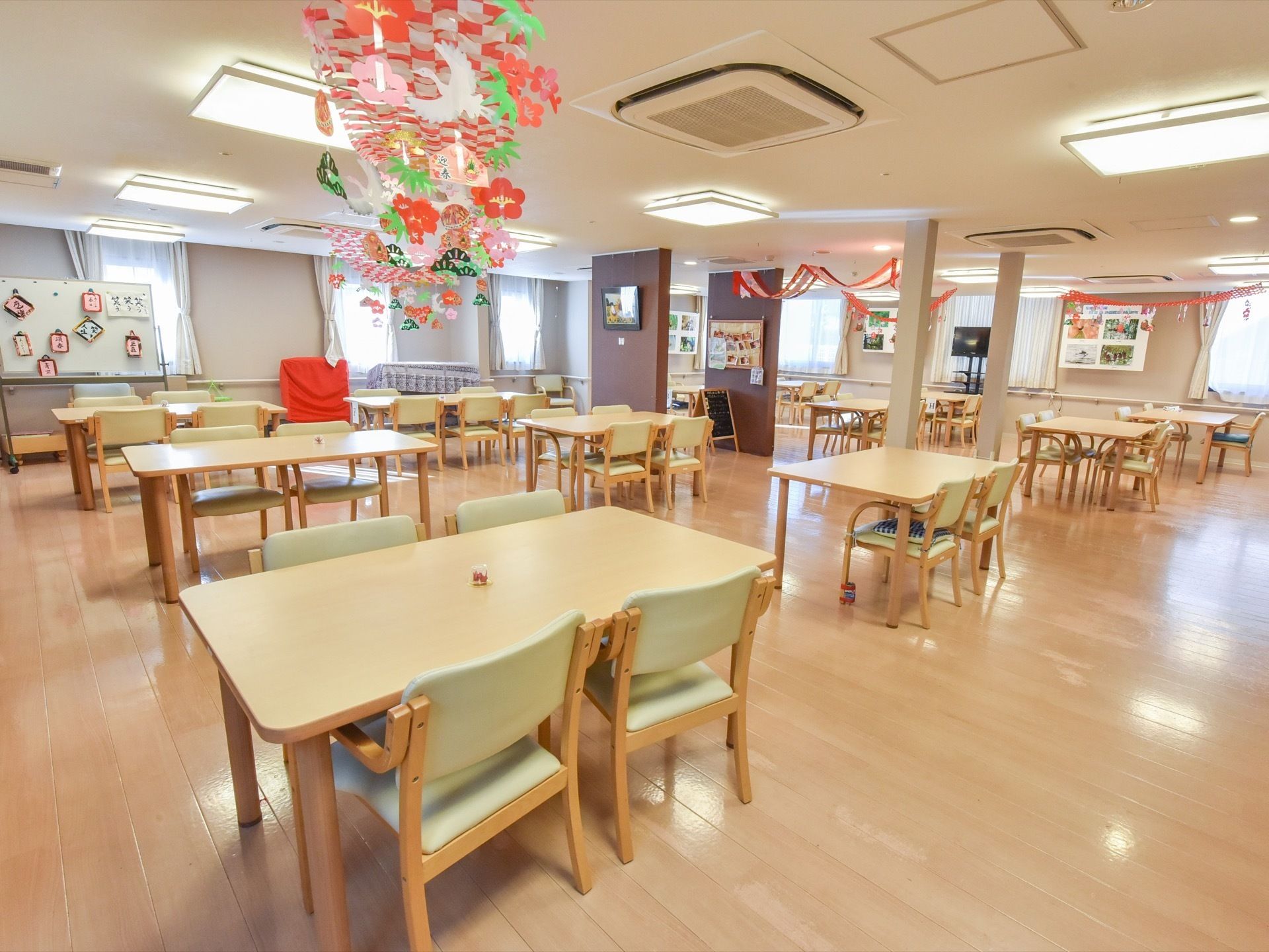 広いリビング内に、10セット以上のテーブルが置かれている。天井には飾りが吊るされており、室内にある柱には写真などが飾られている。