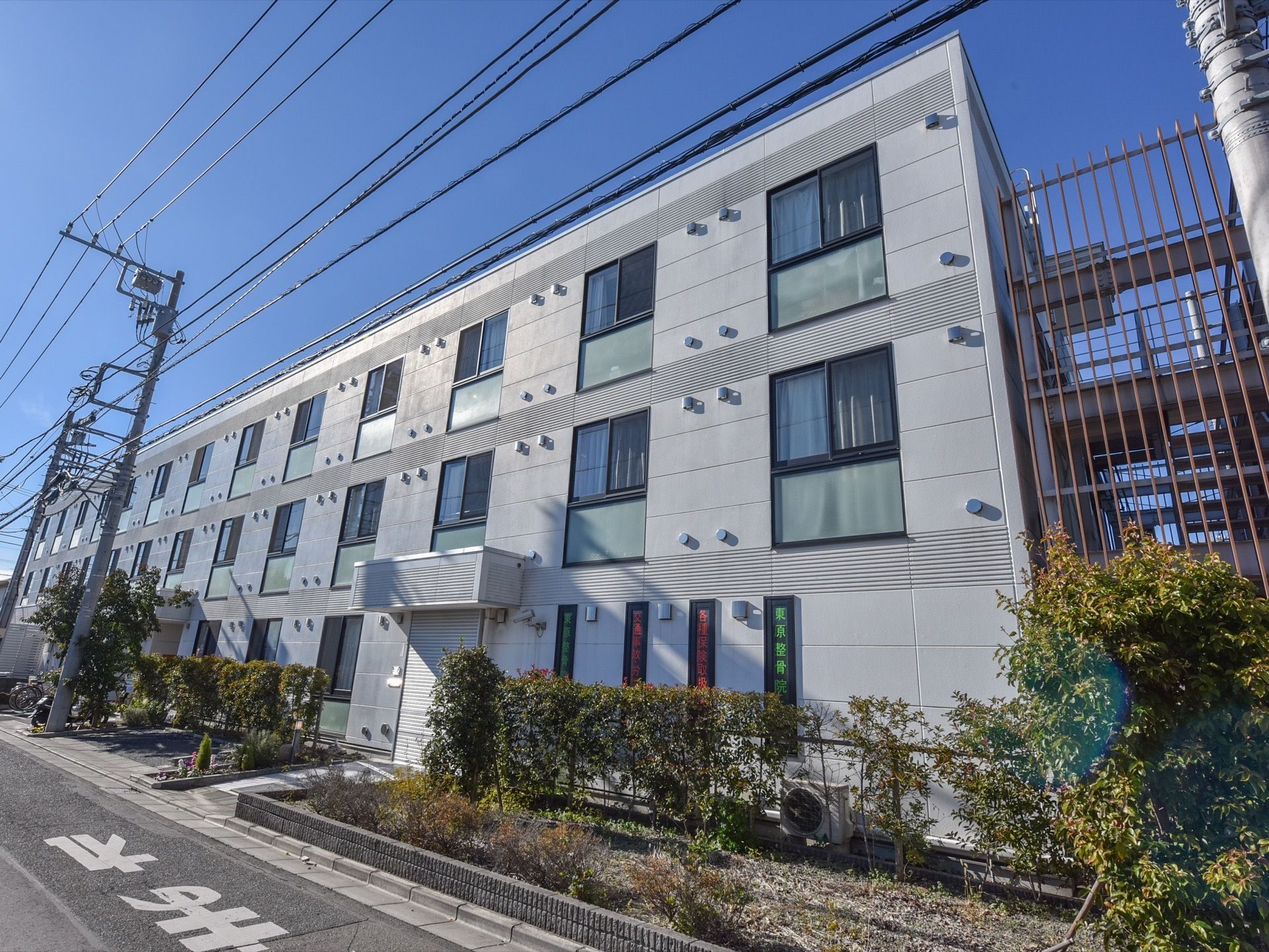 施設の外観である。３階建ての建物で、外階段が付いている。建物沿いに、低木が植えられたスペースが広がっている。