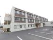 施設の外観は白と茶色の壁の三階建の建物。建物の端には非常階段があり、手前の敷地は駐車場になっている。
