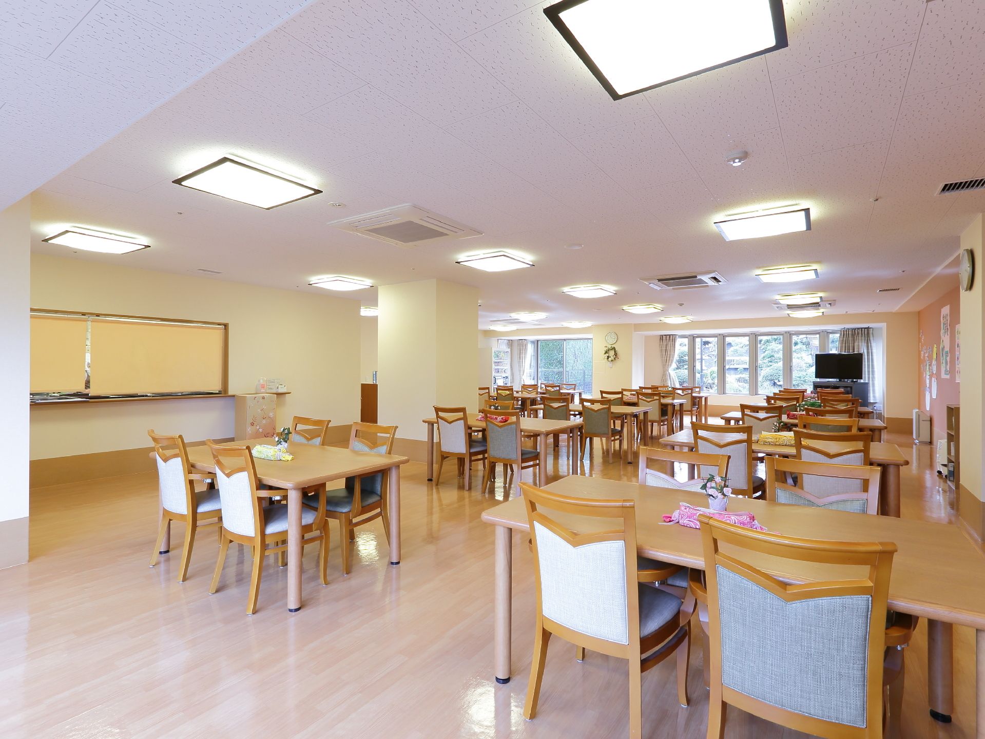 食堂のテーブルは4人掛けがたくさん並んでいて、テーブルの真ん中には小さな花が飾られている。テレビや時計も置いてある。
