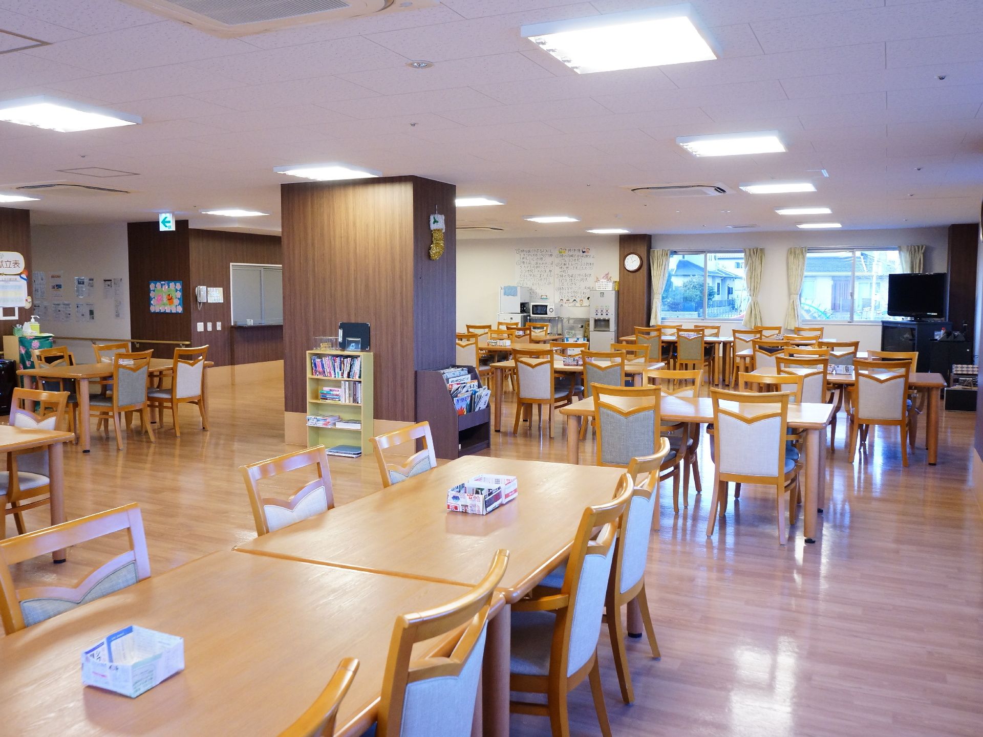 リビングは広いホールになっていて、所々茶色の柱がある。テーブルや椅子が多数置かれていて通路の幅は広く配置されている。