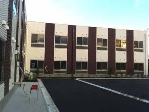 建物の前に赤い灰皿が置かれている、２階建ての白と茶色の外壁が印象的な施設