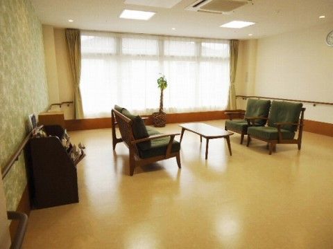 ゆったり広い室内に、4人分のチェアとテーブルが置かれた談話スペースである。大きな窓にはレースのカーテンが掛かっている。