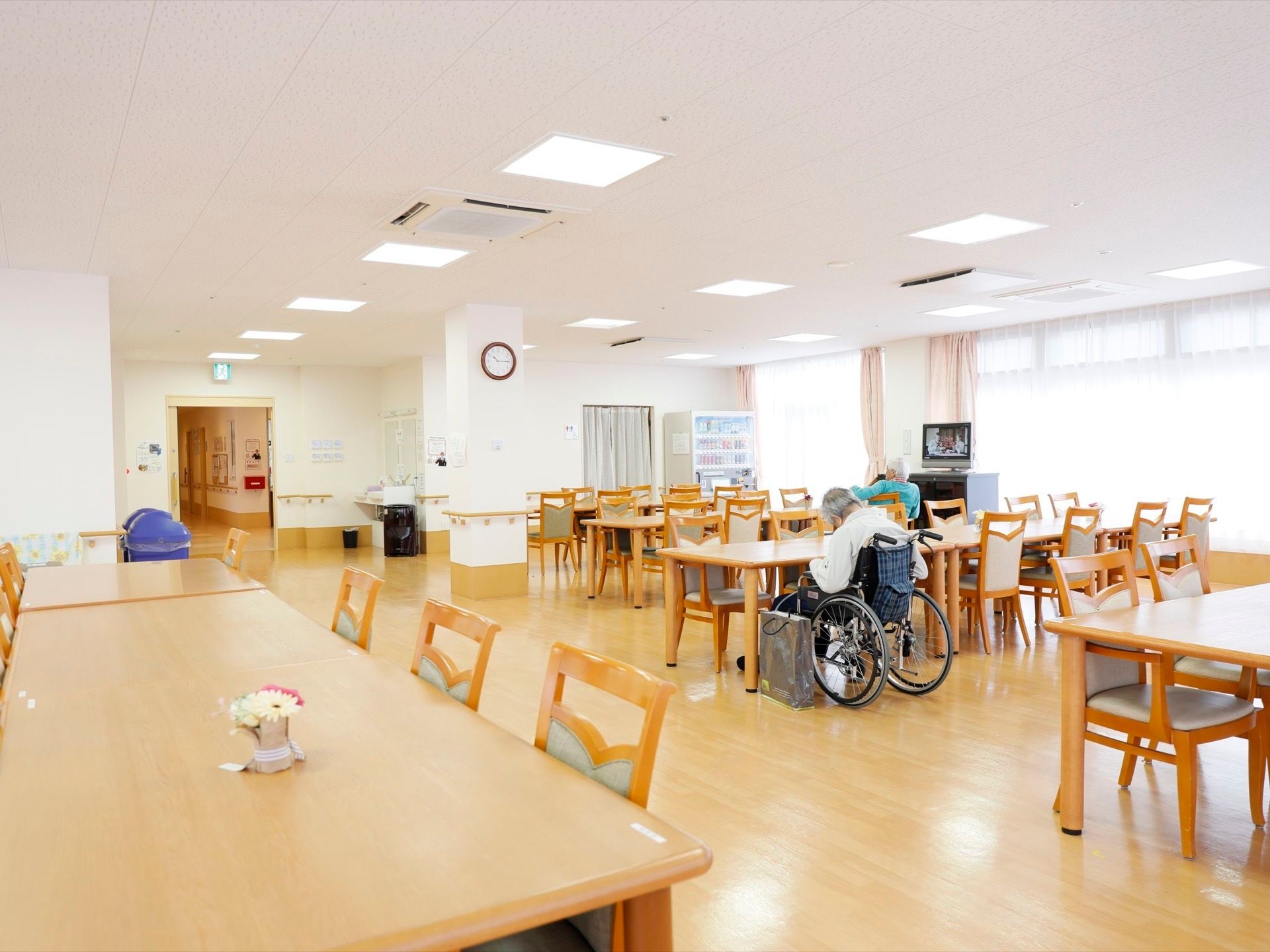 日当たりの良い大きな窓のある部屋。開放的な空間にダイニングテーブル、椅子を多数配置している。テレビ、飲料の自動販売機などがある。