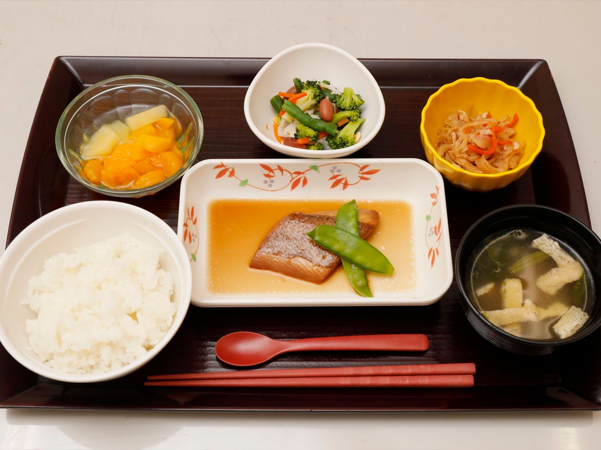 トレイの上に小鉢などに入れられた、いろいろな種類の料理が盛り付けられている。箸が１膳とスプーンが１本置かれている。