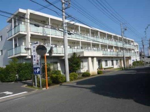 通りに面して横に長く伸びた３階建てで、樹木に囲まれた白い建物