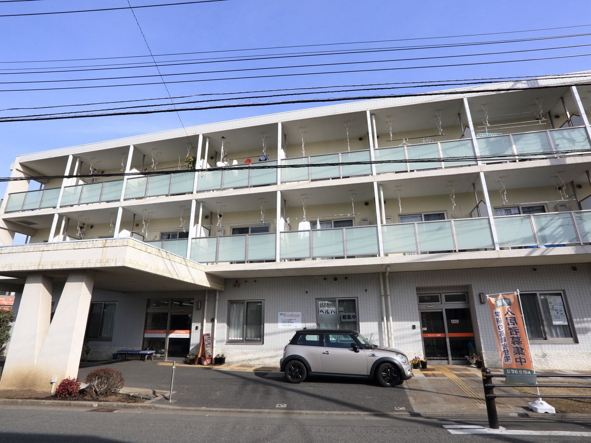 施設の建物は三階建てで、上階にはベランダを設置している。前面には駐車場を設け、玄関へと続く点字ブロックをはめこんでいる。