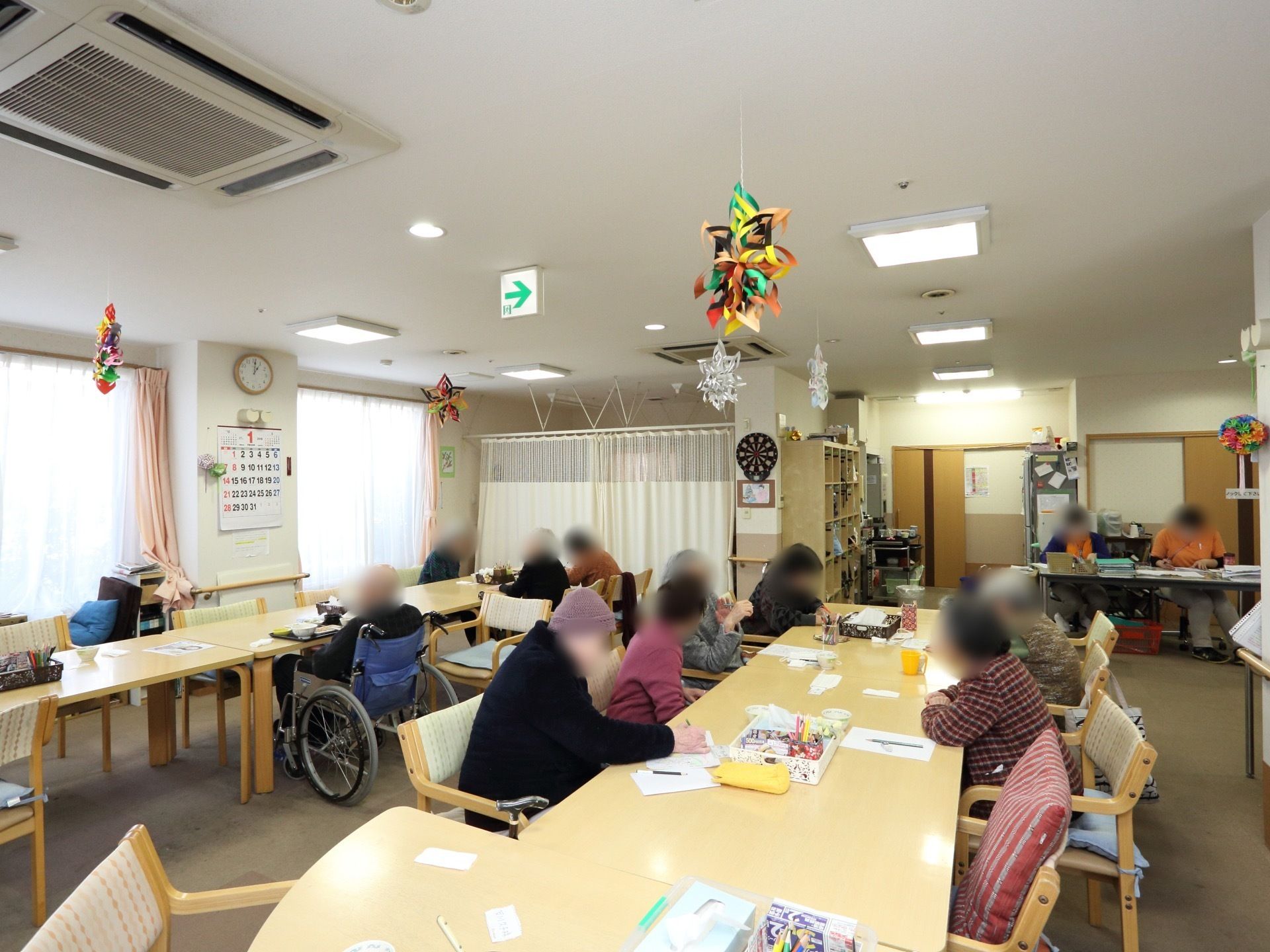 テーブルや椅子が置かれたスペースに、多数の入居者様が集まっている。車椅子でもちょうどいいテーブルの高さである。