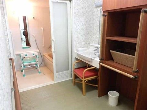 右手の壁際にかごが置かれた棚と洗面台がある個浴用浴室の脱衣所