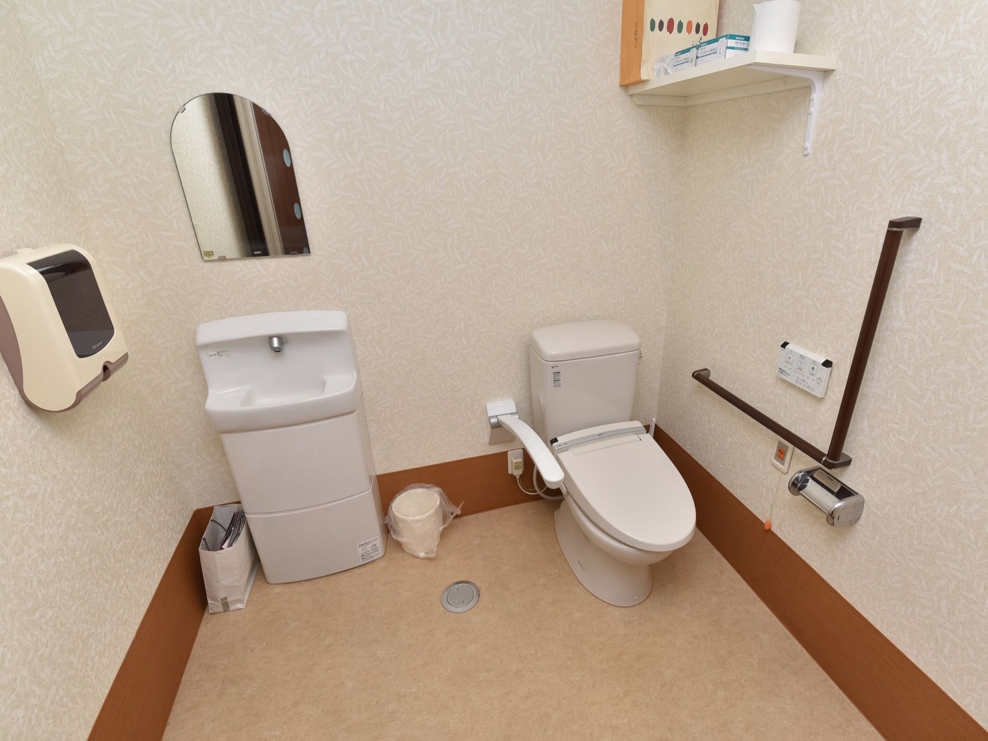 トイレのスペースは広く、洋式トイレと洗面台が並んで設置されている。洋式トイレの左右には手すりやひじ掛けが取り付けられている。