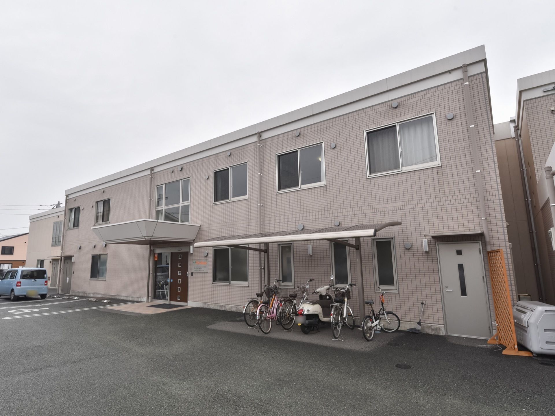 施設の前は舗装されていて屋根が付いた駐輪場や駐車スペースがある。入口前のスペースには大きな屋根が付いている。