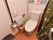 トイレには洋式トイレが設置されている。横の壁にはトイレの操作パネル、L字の手すり、ナースコールが取り付けられている。