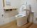 居室のトイレは白壁にフローリングの床。ウォシュレットの水洗トイレ。壁には手すりとスイッチ類。便器の横にも可動式の手すりがある。