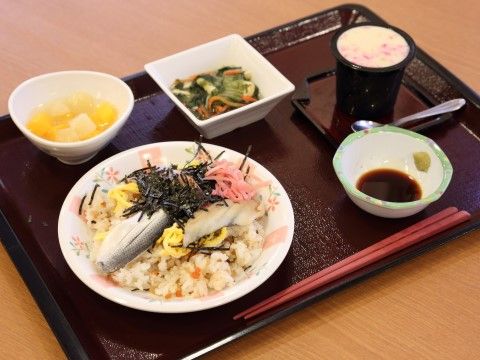 施設の食事は和食が中心のメニュー。魚の切り身の乗ったちらし寿司と煮物、茶碗蒸し、フルーツポンチが配膳されているのが写っている。