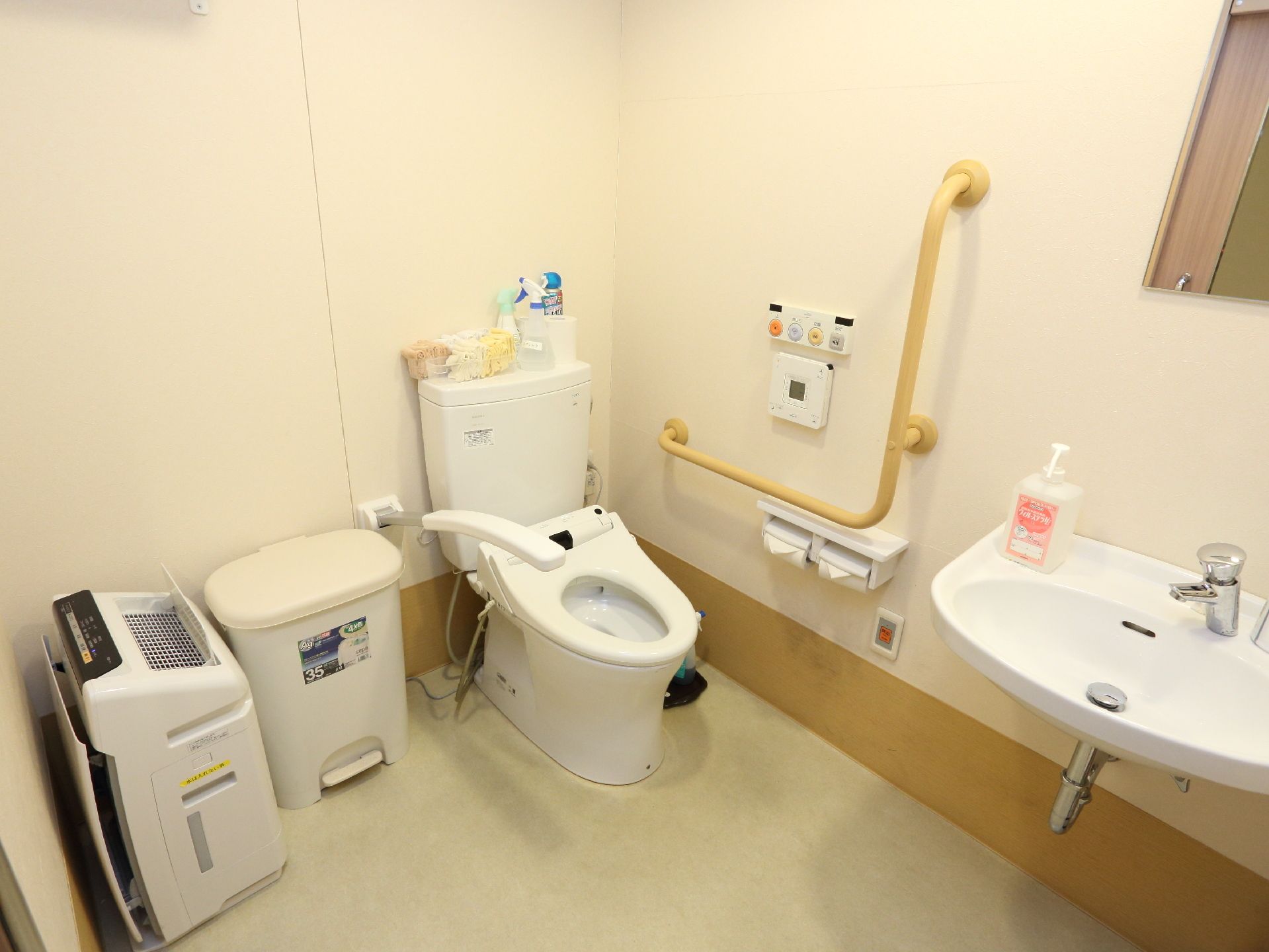 施設のトイレはウォシュレットの水洗トイレ。壁と便器横に手すりがあり、洗面だとゴミ箱、空気清浄機も設置されている。