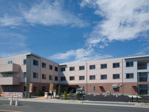 駐車場の奥にあるピンクと茶色に外壁が塗られたＬ字型の建物
