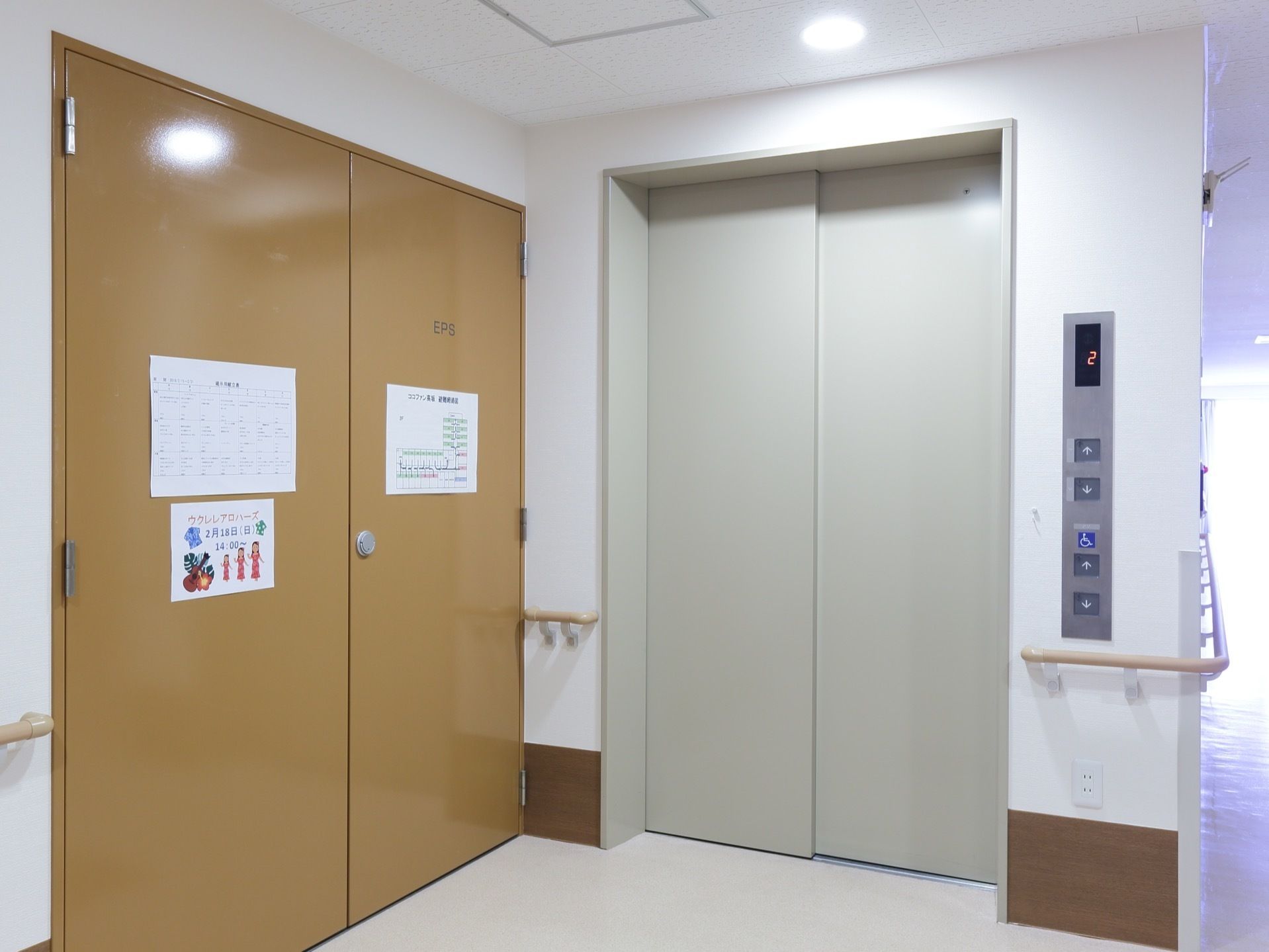 扉の閉まった白いエレベーターが一基設置されている。壁には手すりが付いている。左手には茶色の扉がある。