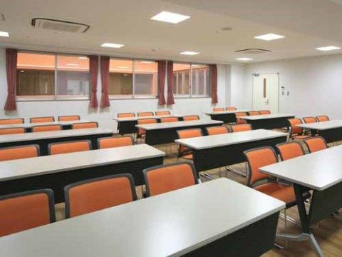 白色の横長テーブル、オレンジ色の椅子が複数並べられた部屋である。入居者様が集まり、いろいろな用途に使用されている。
