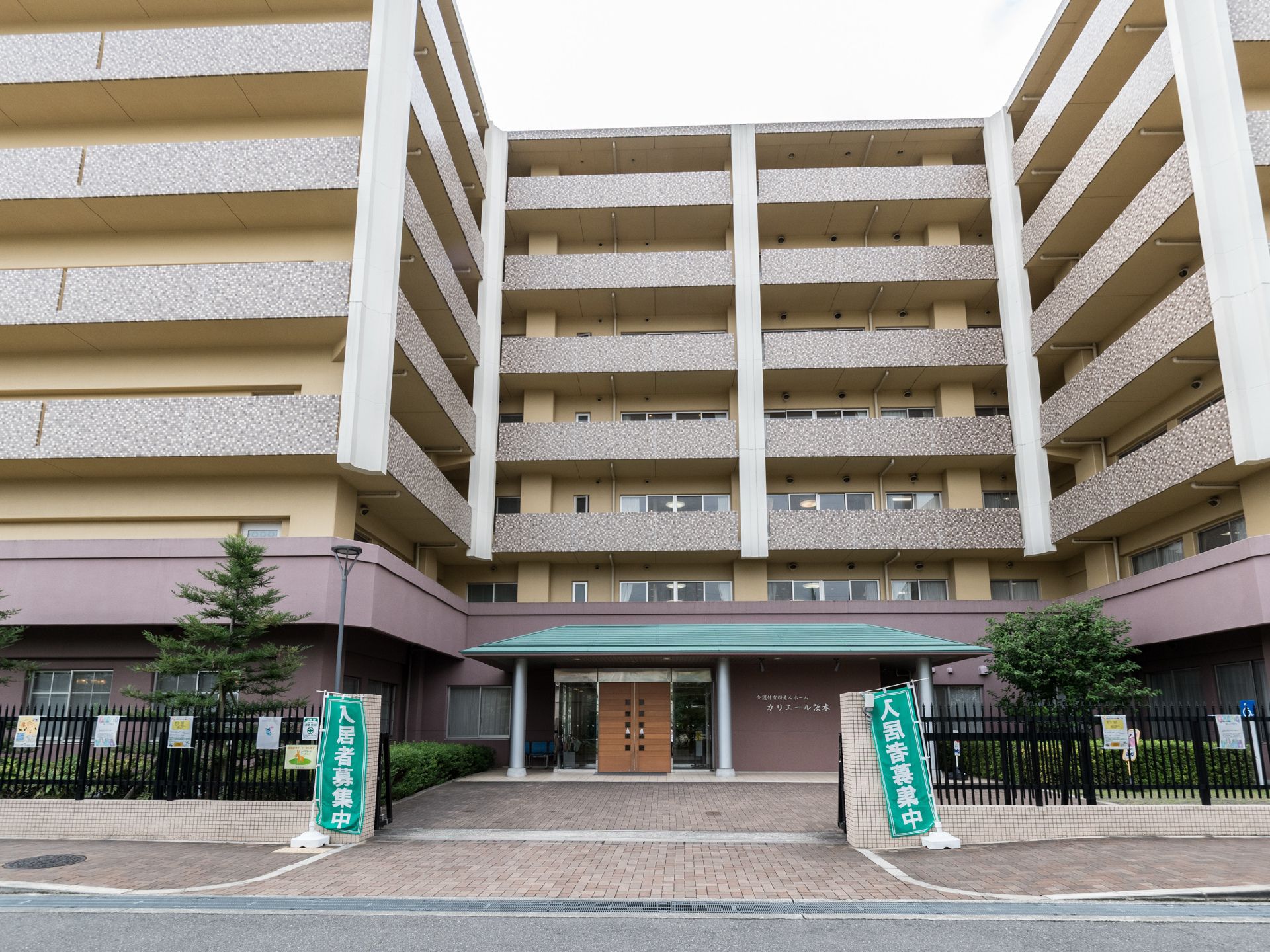 施設は7階建ての茶色い建物である。外周は黒いフェンスで囲われており、入り口の両側には緑色ののぼりが立っている。
