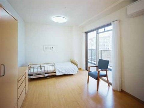 窓の前に落下防止柵のついた介護用ベッドの置かれている縦長の間取りになっている居室
